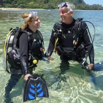 Two scuba divers in full gear standing in the shallow waters of Tunnels Beach in Kauai, Hawaii, captured during an excursion with Fathom Five Divers