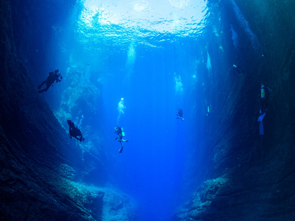 Scuba divers suspended in the deep azure waters during a tour, bubbles rising towards the ocean surface. niihau