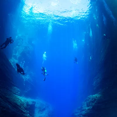 Scuba divers suspended in the deep azure waters during a tour, bubbles rising towards the ocean surface. niihau