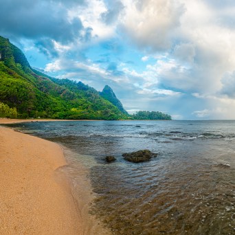 A panoramic view of the sandy shores of Tunnels Beach, Kauai, with mountains in the background, as seen on a trip with Fathom Five Divers