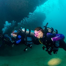 A striking image of three scuba divers swimming in unison at the Sheraton Caverns in Kauai, Hawaii, captured in the style of Zeiss Batis 18mm f/2.8, with hues of dark violet and dark cyan