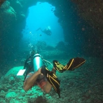 A scuba diver is exploring an underwater cave during an adventurous dive in Kauai, with Fathom Five Divers.