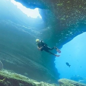 A diver is swimming through a rocky underwater cave during a dive in Tunnels, Kauai, with Fathom Five Divers