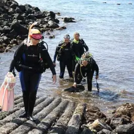 Three scuba divers from Fathom Five Divers walking on a rocky beach at Koloa Landing in Kauai, Hawaii.