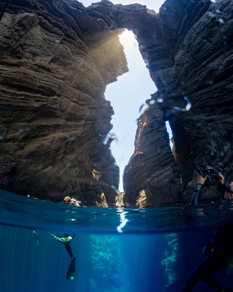 A swimmer exploring underwater caves under a rock in the clear Hawaiian waters near Lehua