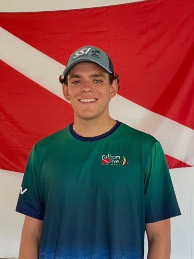 Man in blue cap and green shirt standing in front of red and white diagonal flag.